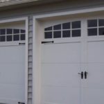 Double white colored garage door with outdoor post lamp